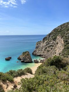 the beach is surrounded by large rocks and clear blue water, with green vegetation on either side