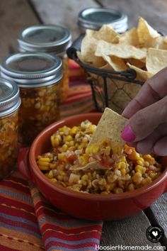 a person dipping tortilla chips into a bowl full of mexican corn and salsa