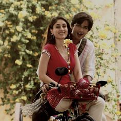 a man and woman riding on the back of a motorcycle with flowers in the basket