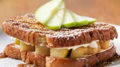 a white plate topped with two sandwiches covered in apple slices and powdered sugar on top of each other