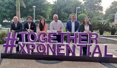 four people posing in front of a sign that says together exponental with purple letters