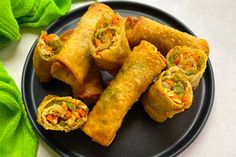 a black plate topped with vegetable spring rolls