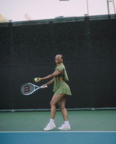 a woman holding a tennis racquet on top of a tennis court with a ball in her hand