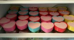 many heart shaped candles are on display in a glass case with white shelves behind them