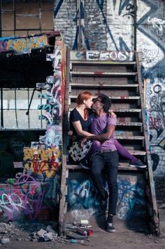 a man and woman sitting on top of a step case in front of graffiti covered wall