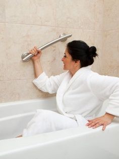 a woman sitting in a bathtub holding onto the handle of a faucet