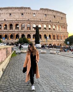 a woman walking down a cobblestone street in front of an old building with the roman colossion behind her