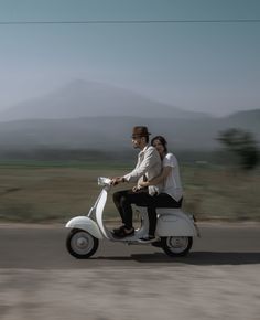 a man and woman riding on the back of a scooter down a road