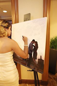 a woman in a white dress is writing on a large board with a man standing next to her