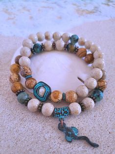 Get those sandy vibes flowing with our Beachy Bracelets, featuring natural stones, patina green accents, pearls, and cute ocean-inspired charms. Here you can choose between a "Caged Pearl" or a pretty Stingray as a charm. Or get one of each since they work great stacked too! I use grounding and balancing Picture Jasper, African Turquoise to bring positive energy, and River Stone to invigorate your aura and facilitate going with the flow. Each bracelet in my Mykonos Collection features antiqued patina charms and spacers made in Greece, where the art of metal finishing was popular already thousands of years ago. Pearls, stingrays, shells, and other fun shapes adorn this always-evolving collection. I make these quality bracelets in-house, using the most robust elastic available with double kn Beachy Bracelets, Bold Boho, Patina Green, Ocean Bracelet, Ocean Inspired Jewelry, Beach Bracelets, Beads Bracelet Design, Ocean Inspired, Natural Stone Bracelets