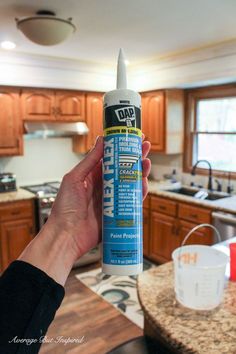 a person holding up a bottle of glue in a kitchen