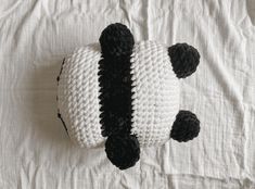 a knitted panda bear laying on top of a bed with white and black sheets