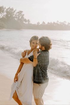 two people standing on the beach hugging each other