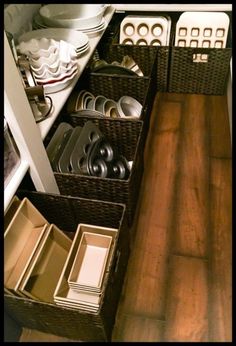 an organized kitchen with wooden floors and white dishes in baskets on the bottom shelf next to drawers