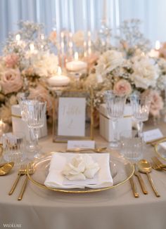 the table is set with white and gold place settings, silverware, and flowers