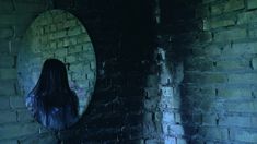 a woman standing in front of a brick wall with a mirror on it's side