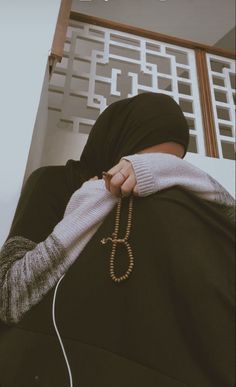 a woman in a black hijab is holding on to a brown beaded necklace