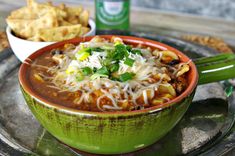 a green bowl filled with chili and cheese on top of a metal tray next to crackers