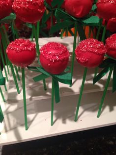 red cake pops with sprinkles on them sitting in front of green stems