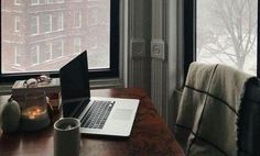 an open laptop computer sitting on top of a wooden desk next to a cup and candle