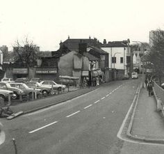 an old black and white photo of cars parked on the side of a road in front of buildings