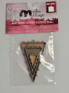 a small triangle shaped brooch with rivets on it's side in a package