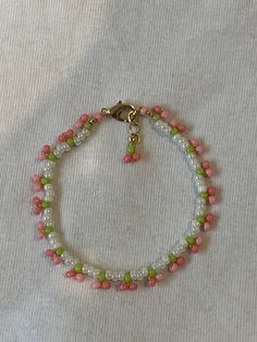 a pink and green beaded bracelet on a white surface with a gold charm hanging from the clasp