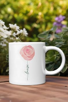 a white coffee mug sitting on top of a wooden table next to flowers and greenery