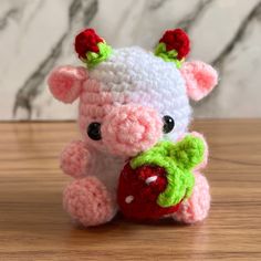 a small crocheted pig holding a heart on top of a wooden table next to a marble wall