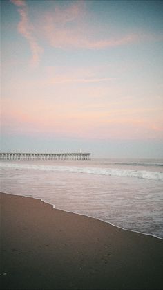 a person walking on the beach with a surfboard in hand and a pier in the background