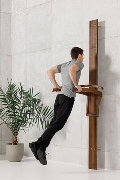 a man leaning against a wall with his hands on the back of a wooden chair