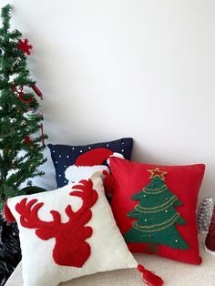 three christmas pillows sitting on top of a white couch next to a small christmas tree