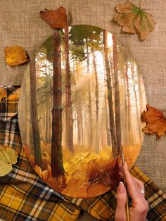 a person is painting trees in the woods on a paper plate with leaves around it