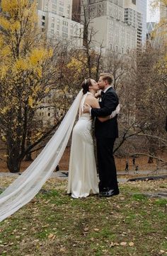 a bride and groom kissing in front of the city skyline with their veil blowing in the wind