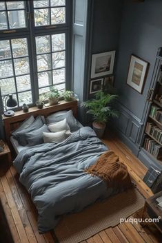 a bed sitting under a window next to a book shelf in a room with wooden floors