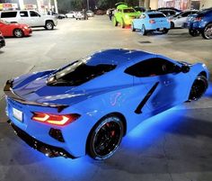 a blue sports car parked in a parking lot with other cars behind it at night