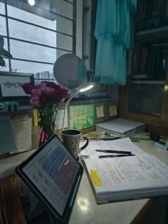 an open book on a desk next to a tablet computer and flowers in a vase