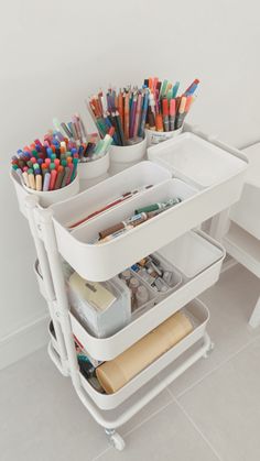 a white desk with lots of pens and pencils in it's holder on wheels