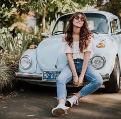 a woman sitting on the hood of an old car