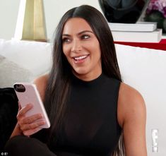 a woman sitting on a couch holding a cell phone in her hand and looking at the camera