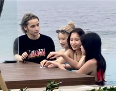 four young people sitting at a table near the water