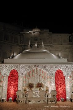 an elaborately decorated stage set up for a wedding at night with red flowers on the walls