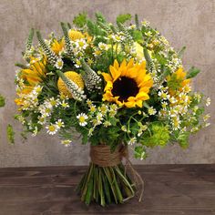 a bouquet of sunflowers and daisies in a vase on a wooden table