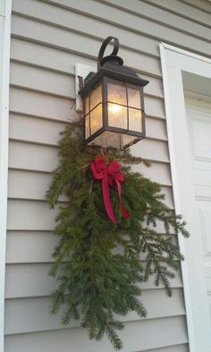 a lantern hanging from the side of a house with a red bow on it's front door