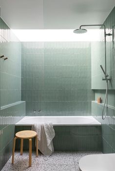 a green tiled bathroom with a bathtub and stool