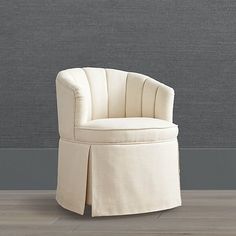 an upholstered chair with pleated skirting on the bottom and back, in front of a gray wall