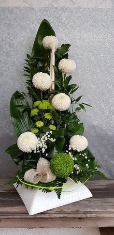 white flowers and greenery are arranged in a triangle arrangement on a wooden table with a gray wall behind it