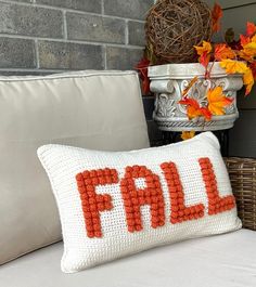 a pillow with the word fall written on it sitting next to a basket full of autumn leaves