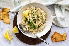 a white bowl filled with food next to crackers and lemon wedges