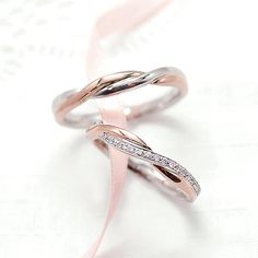 two wedding bands with diamonds on them sitting on a pink ribbon and white paper background